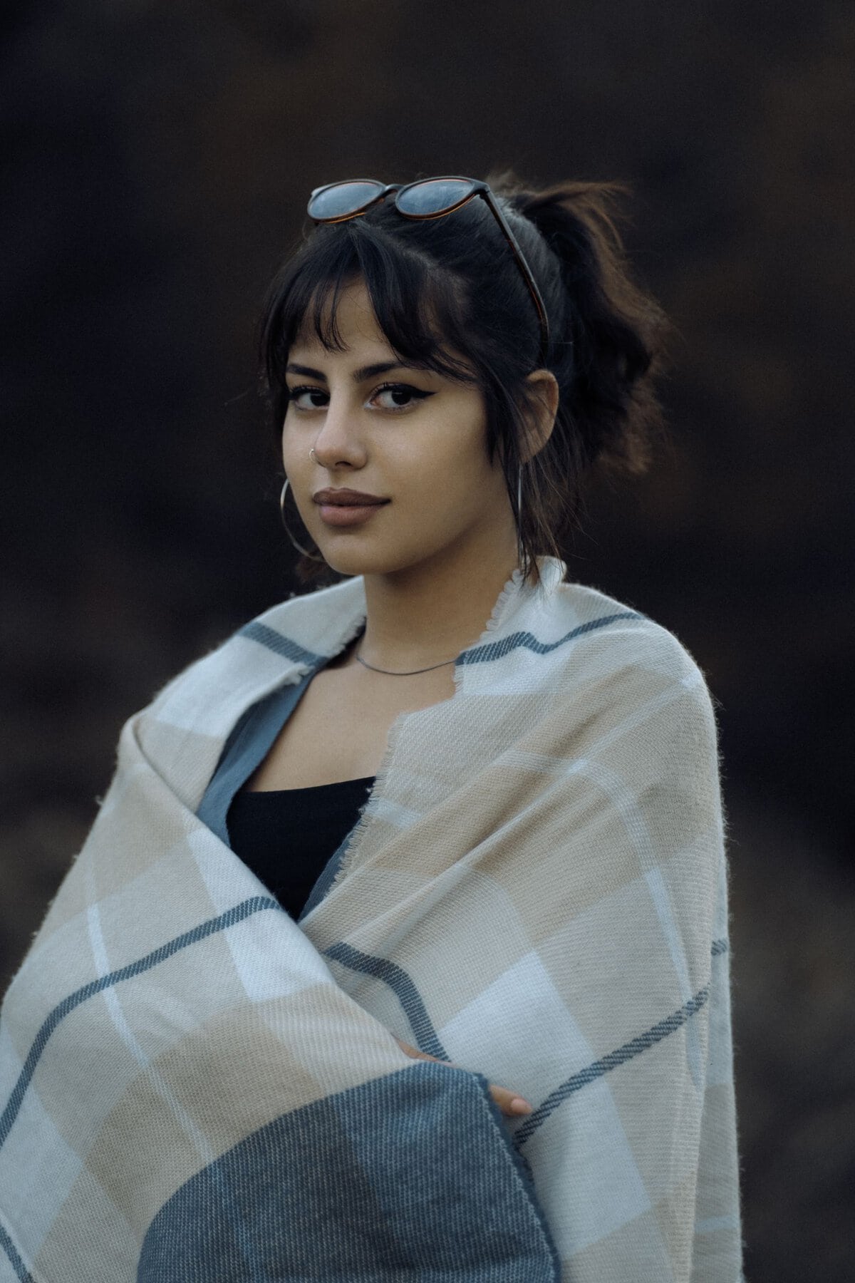 Elegant young woman wrapped in a scarf with sunglasses resting on her head.