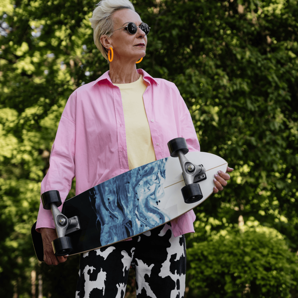 older woman holds a skateboard while wearing a colorful, playful outfit