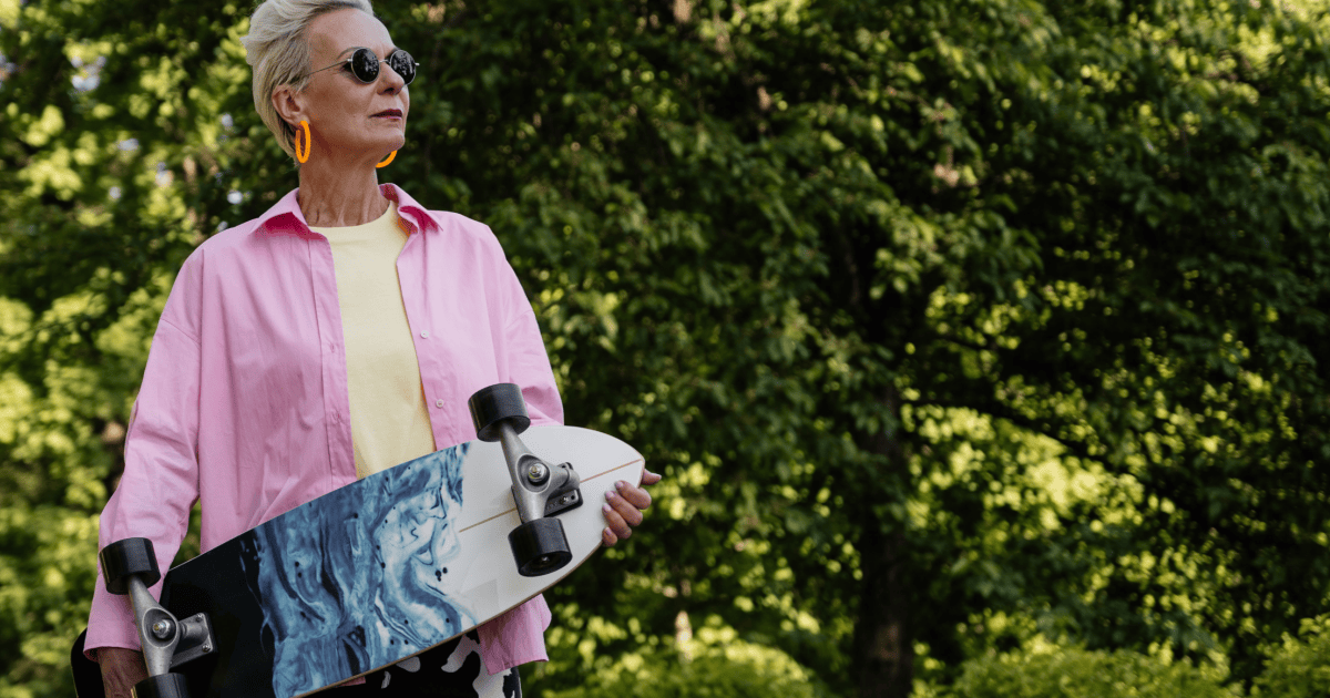 older woman holds a skateboard while wearing a colorful, playful outfit