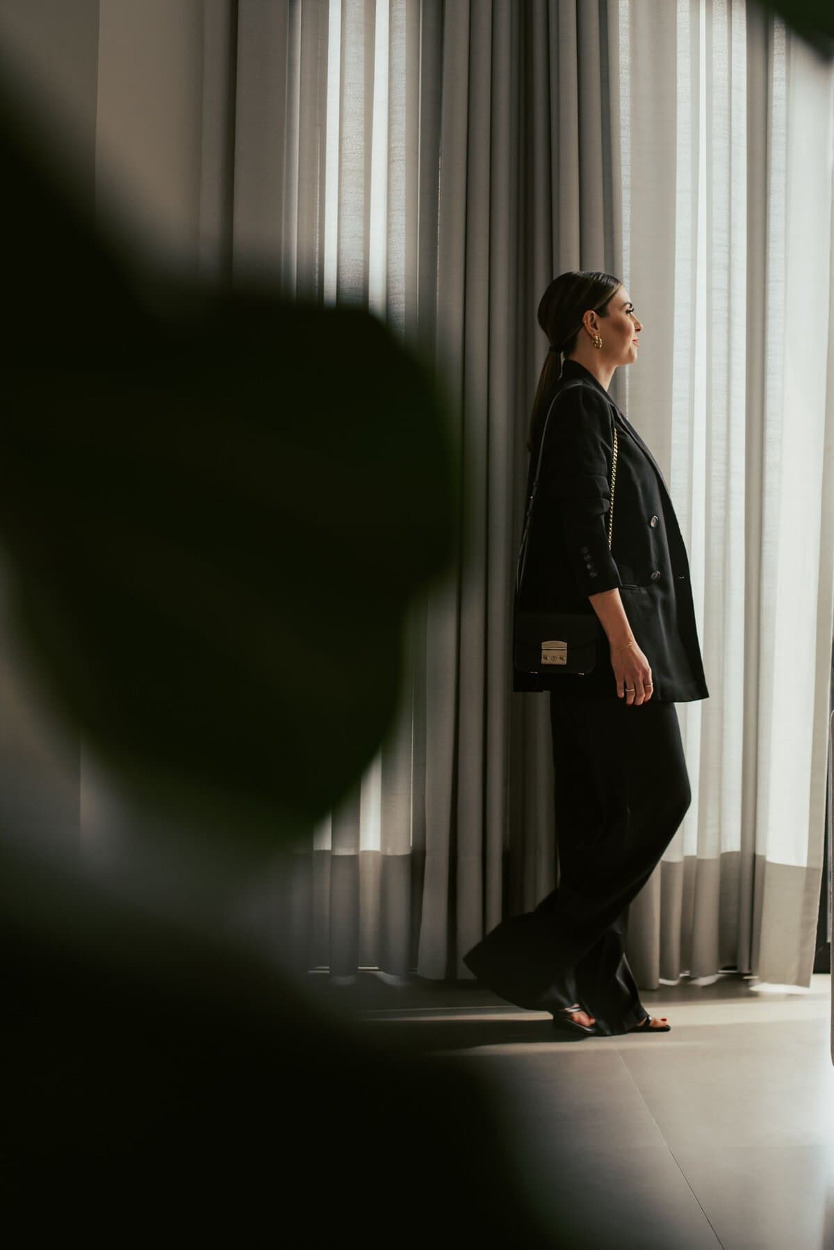 Stylish woman standing elegantly in a sunlit room with curtains.
