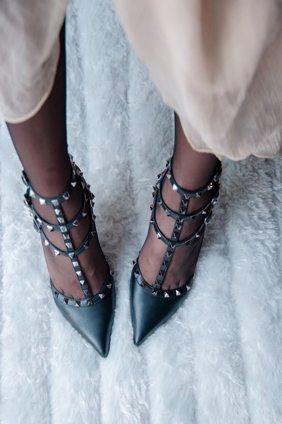 Top view of fashionable black studded high heels worn by a woman on a fluffy rug.